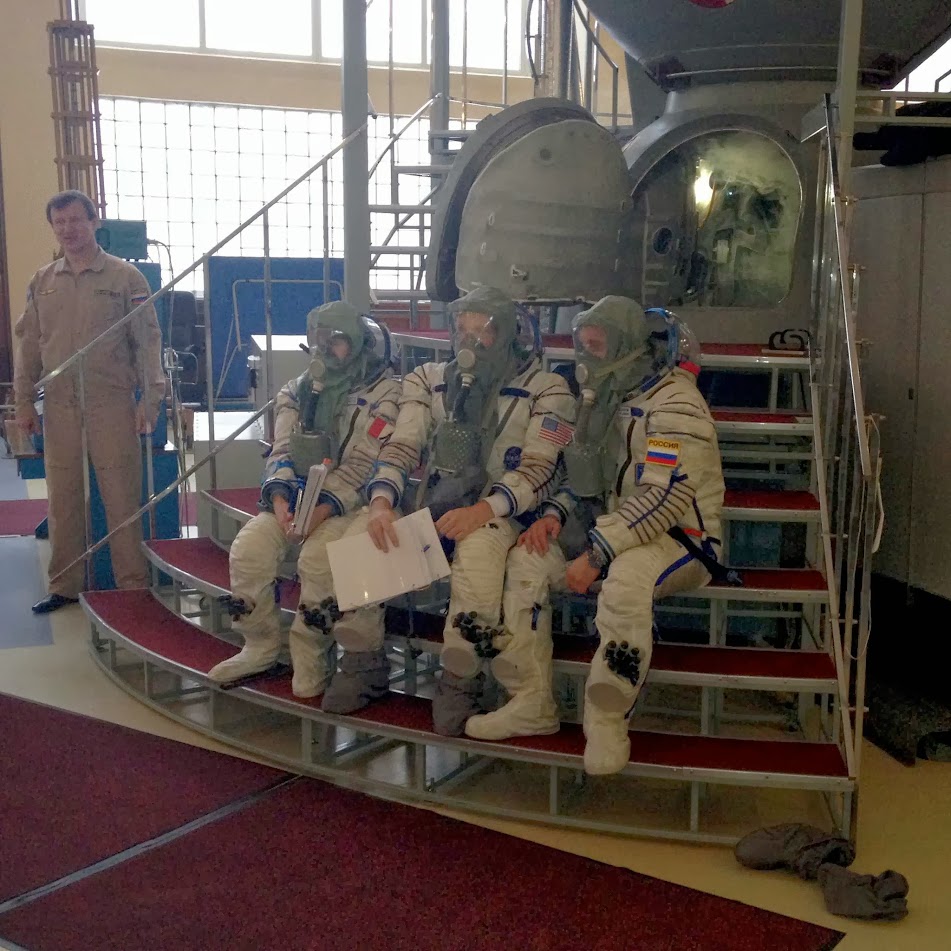 L'équipage de l'expédition 42 assis devant le simulateur Soyouz en combinaison Sokol et masque à gaz